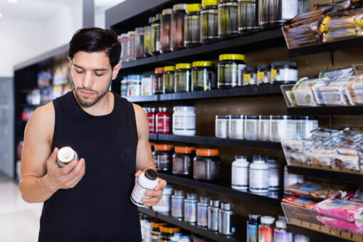 Serious efficient young muscular man choosing sport nutrition products in shop