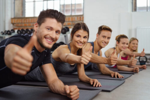 Group of men and women give the camera a thumbs up while on yoga mats in sports gym
